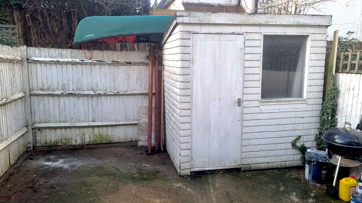 View of the bottom of the garden, white fencing and an old looking shed.